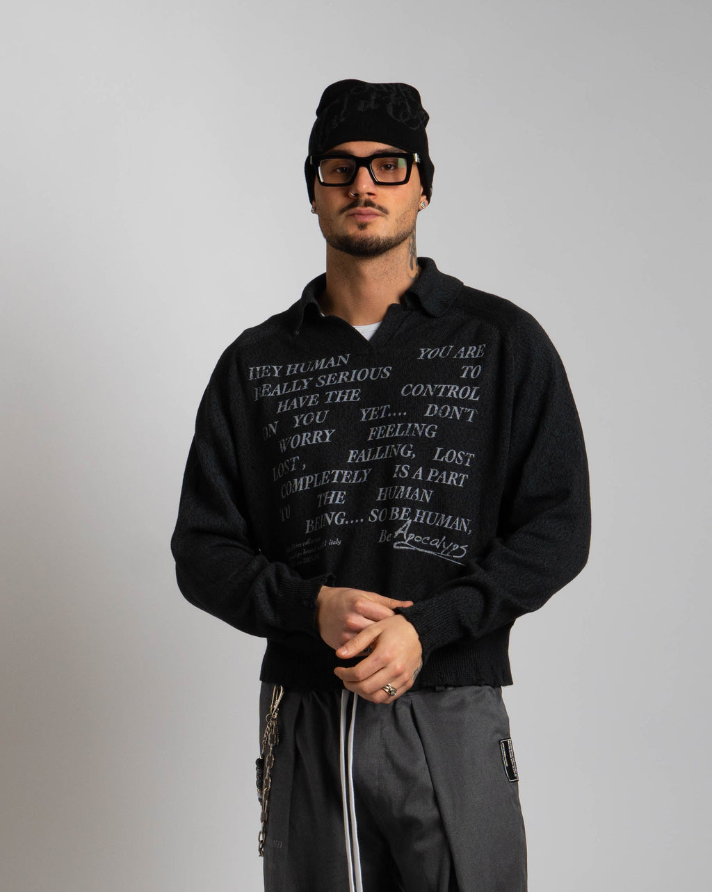 Person wearing a black hoodie and pants with text, standing on a textured surface.