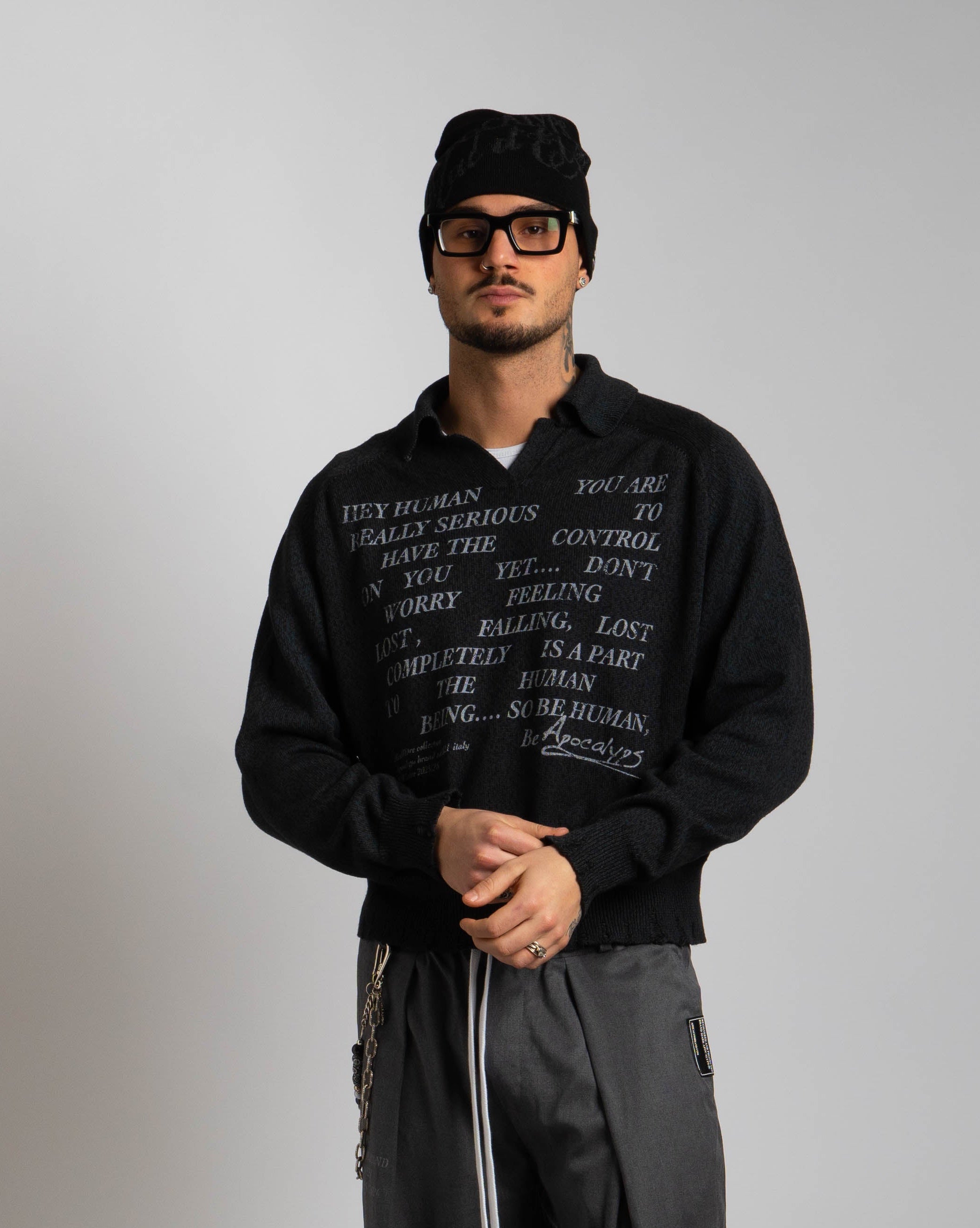 Person wearing a black hoodie and pants with text, standing on a textured surface.