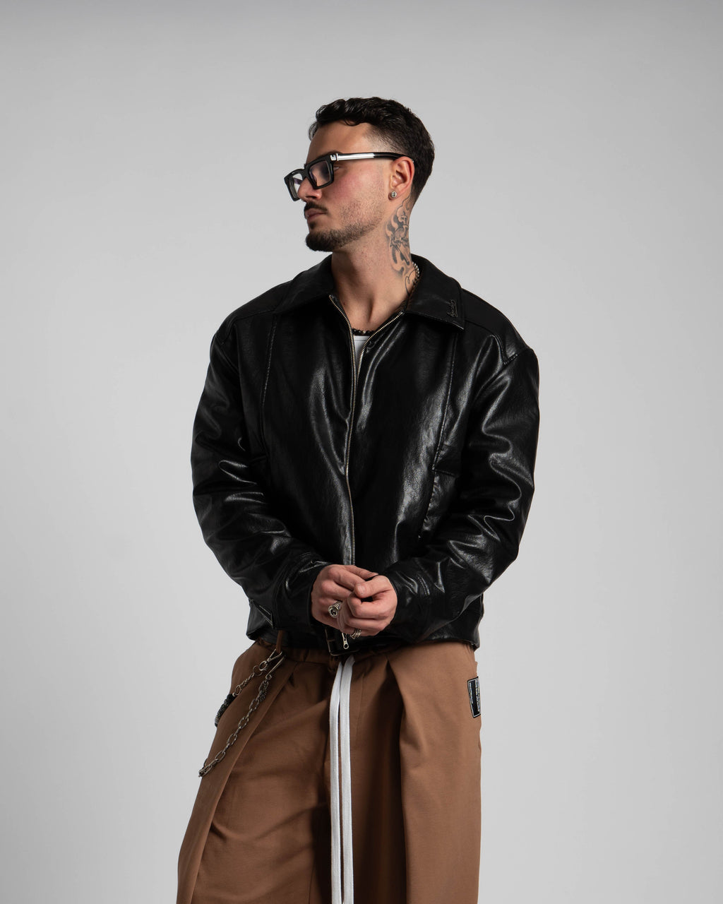 Man wearing a black leather jacket and brown pants against a plain background
