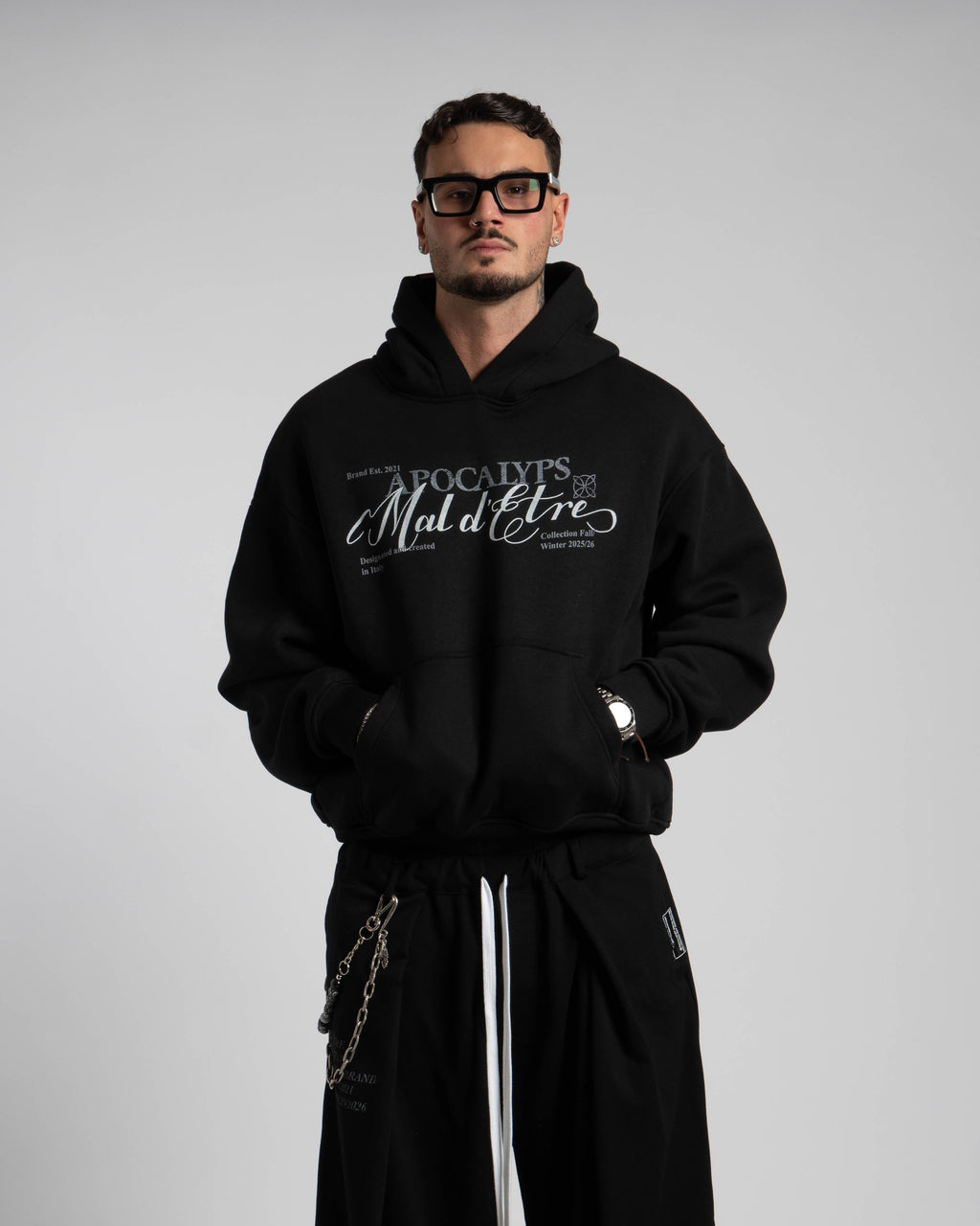 Man wearing a black hoodie with text and black pants on a plain background