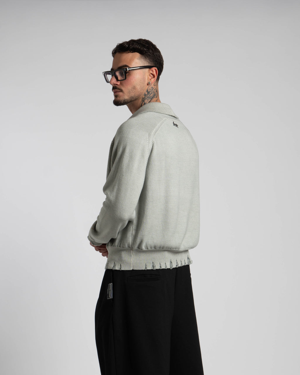 Man wearing a light gray sweater and black pants on a plain background