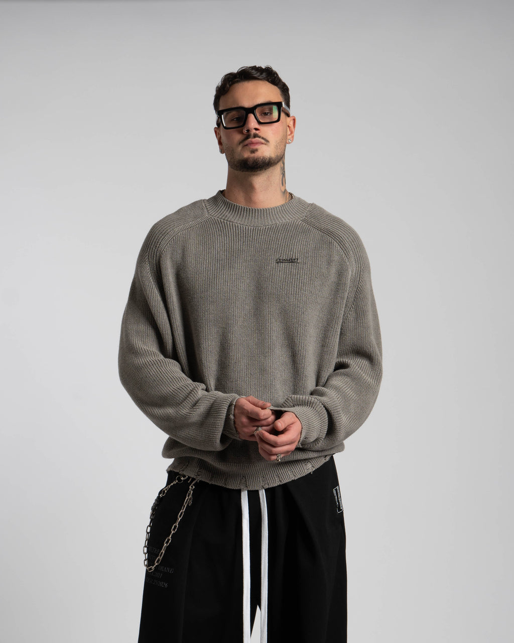 Man wearing a gray sweater and black pants against a plain background